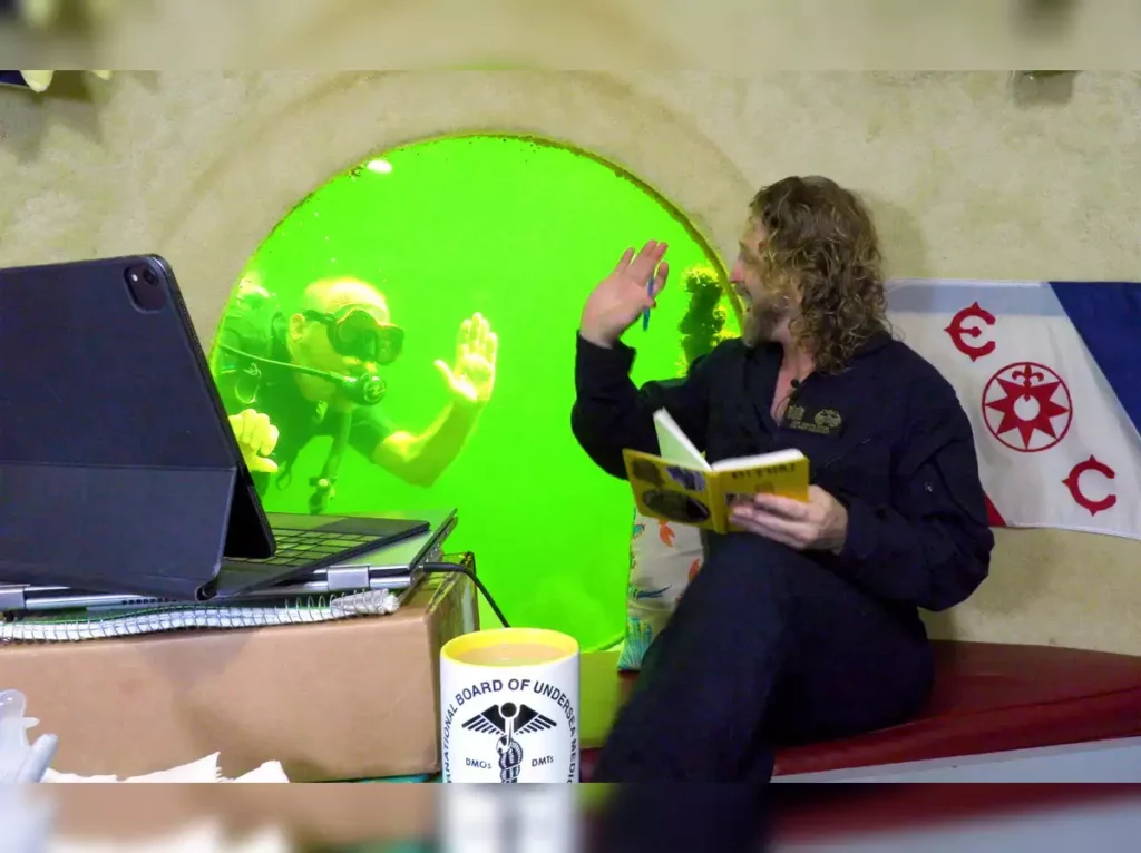 Man reading a book while a scuba diver swims by and waves