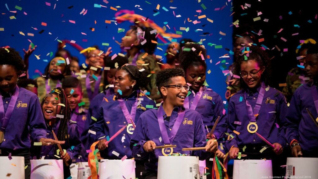 Several Kids Drumming with Medals around their neck and confetti falling on them