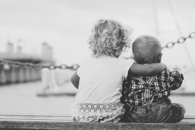 Black and White photo of two kids with their back towards the camera sitting and hugging eachother