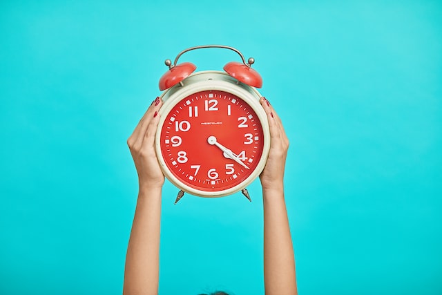 Two hands holding up an alarm clock with a blue background