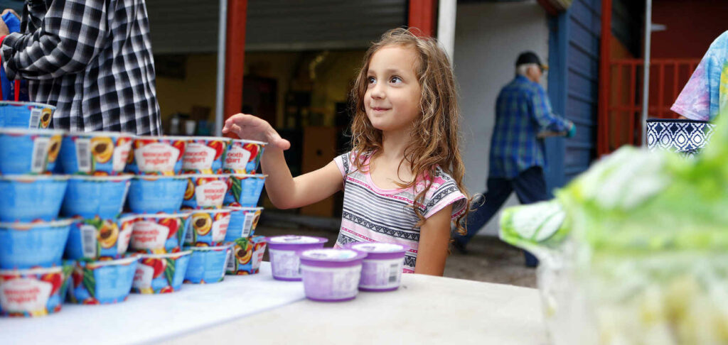 A little girl grabbing mac n cheese at a foodbank