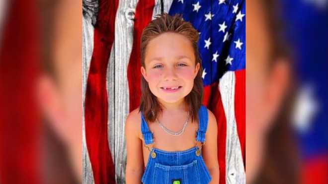 A little boy with a mullet in overalls